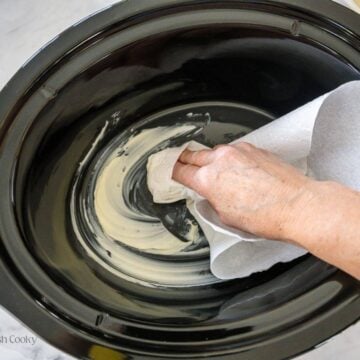 Hand greasing the crock pot insert with butter using a paper towel.