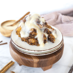 Crock pot cinnamon roll casserole on plates with cream cheese frosting drizzled on top.