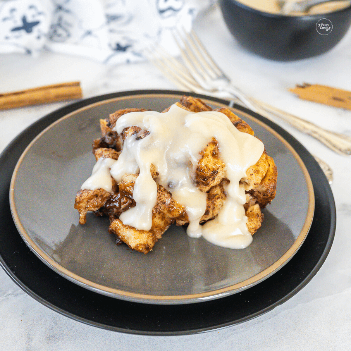 Crock pot cinnamon roll casserole serving on a plate drizzled with creamy cream cheese frosting.