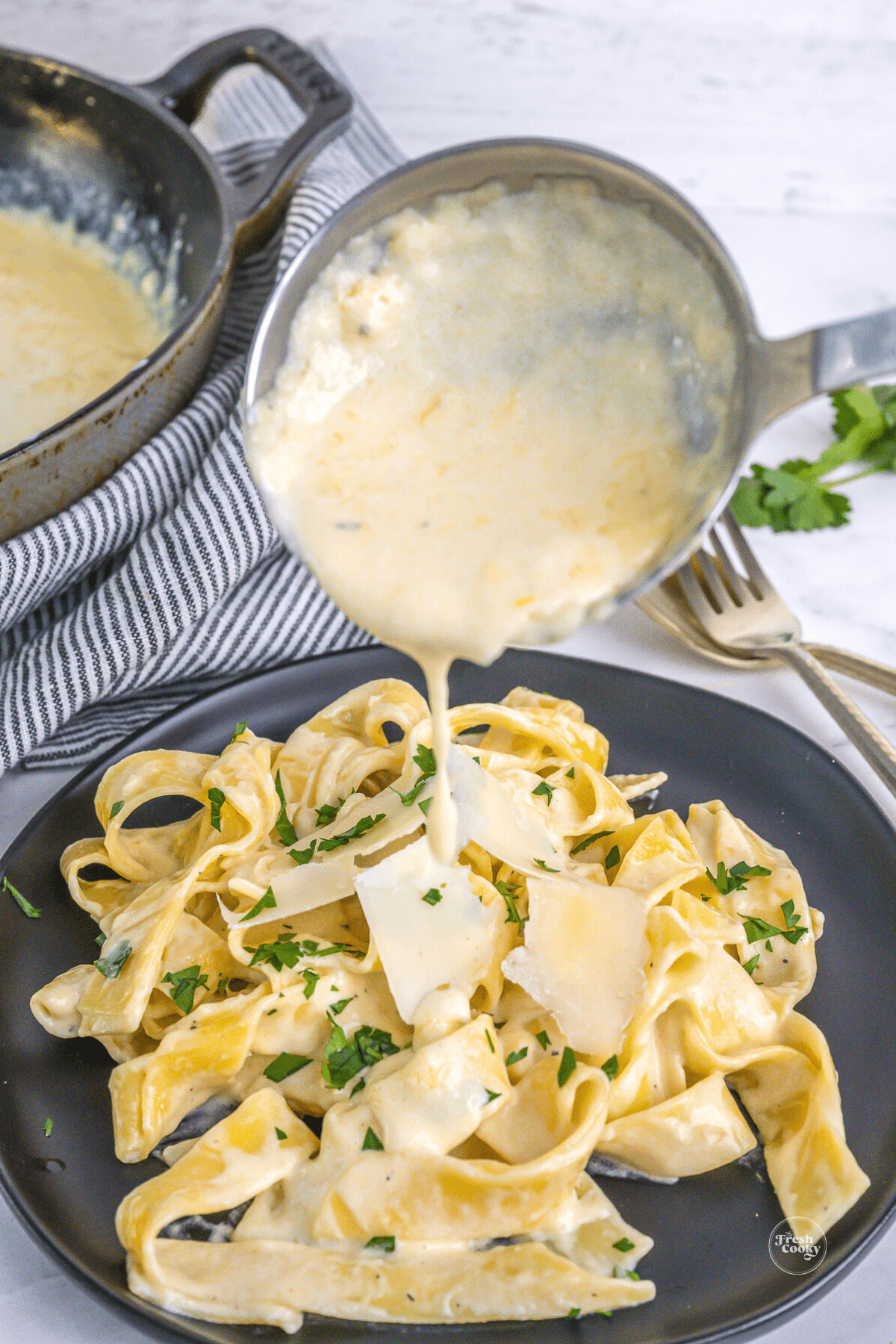 Ladling alfredo sauce onto the fresh fettuccine.