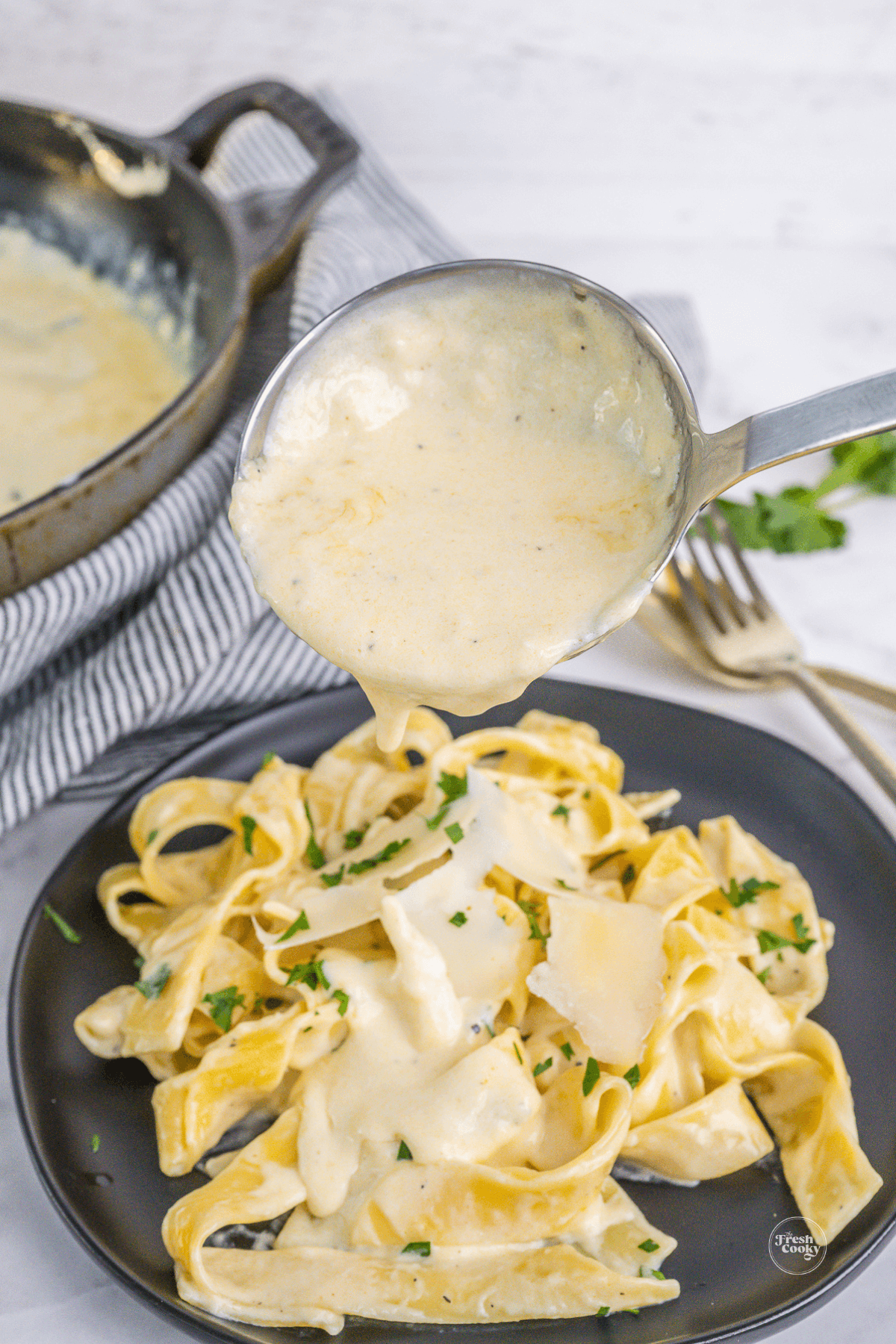 Spooning homemade alfredo sauce over fettuccine.