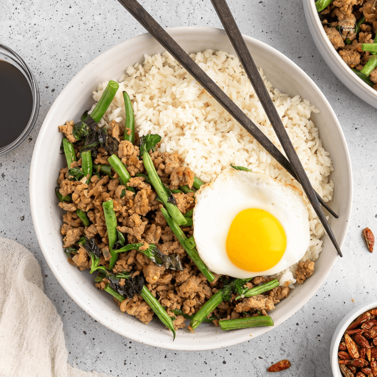 Pad Kra Pao Thai Ground Pork Stir Fry with Thai fried egg with rice in a bowl with chop sticks.