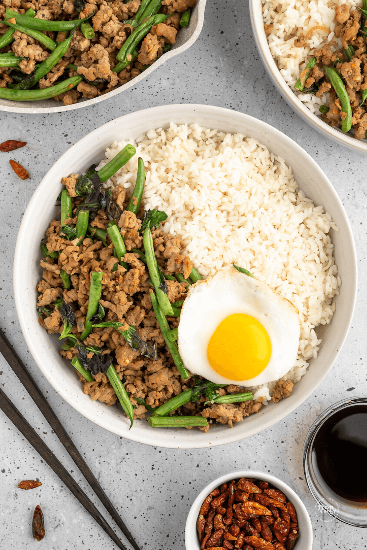 Bowl filled with ground pork stir fry, Jasmine rice, topped with Holy Basil and a Thai fried egg.