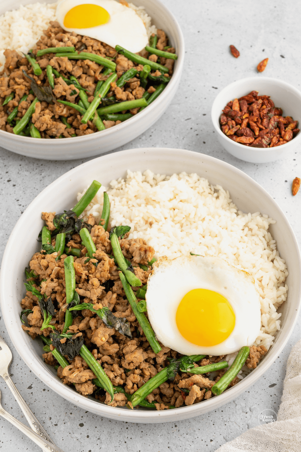 Ground pork stir fry with Thai Holy Basil and fried egg with another individual serving in background.