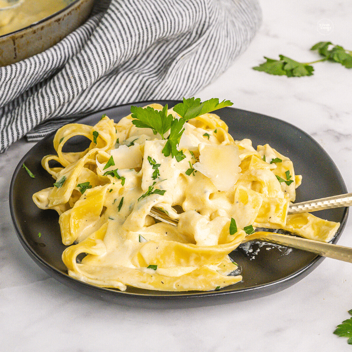 Homemade Alfredo sauce recipe without cream cheese spooned onto fettuccine on black plate.