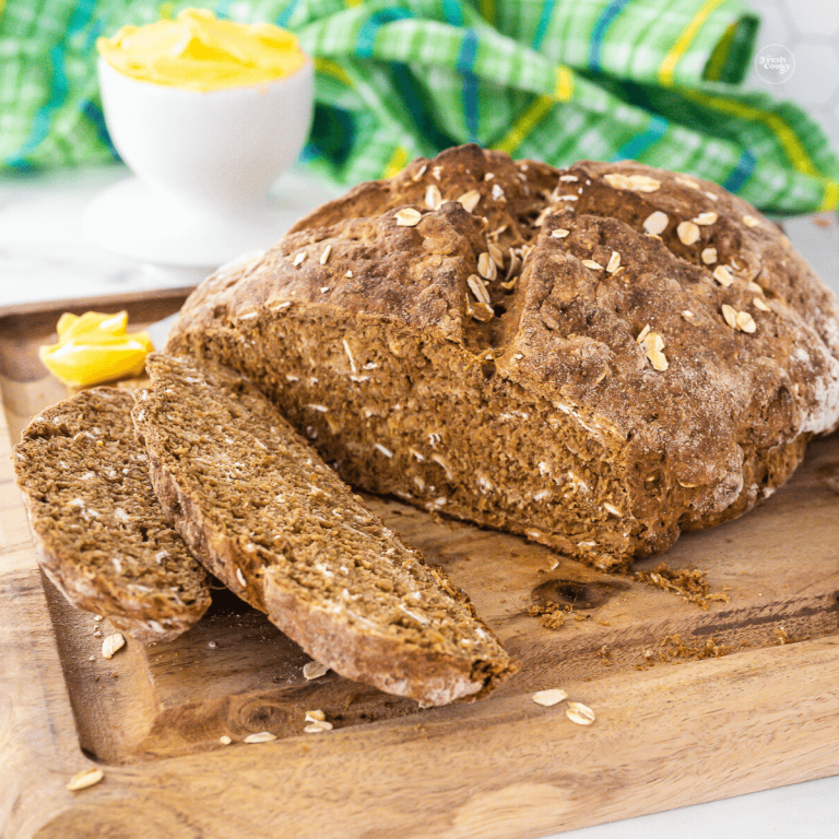 Irish brown soda bread recipe on cutting board with a few pieces sliced, butter in background.