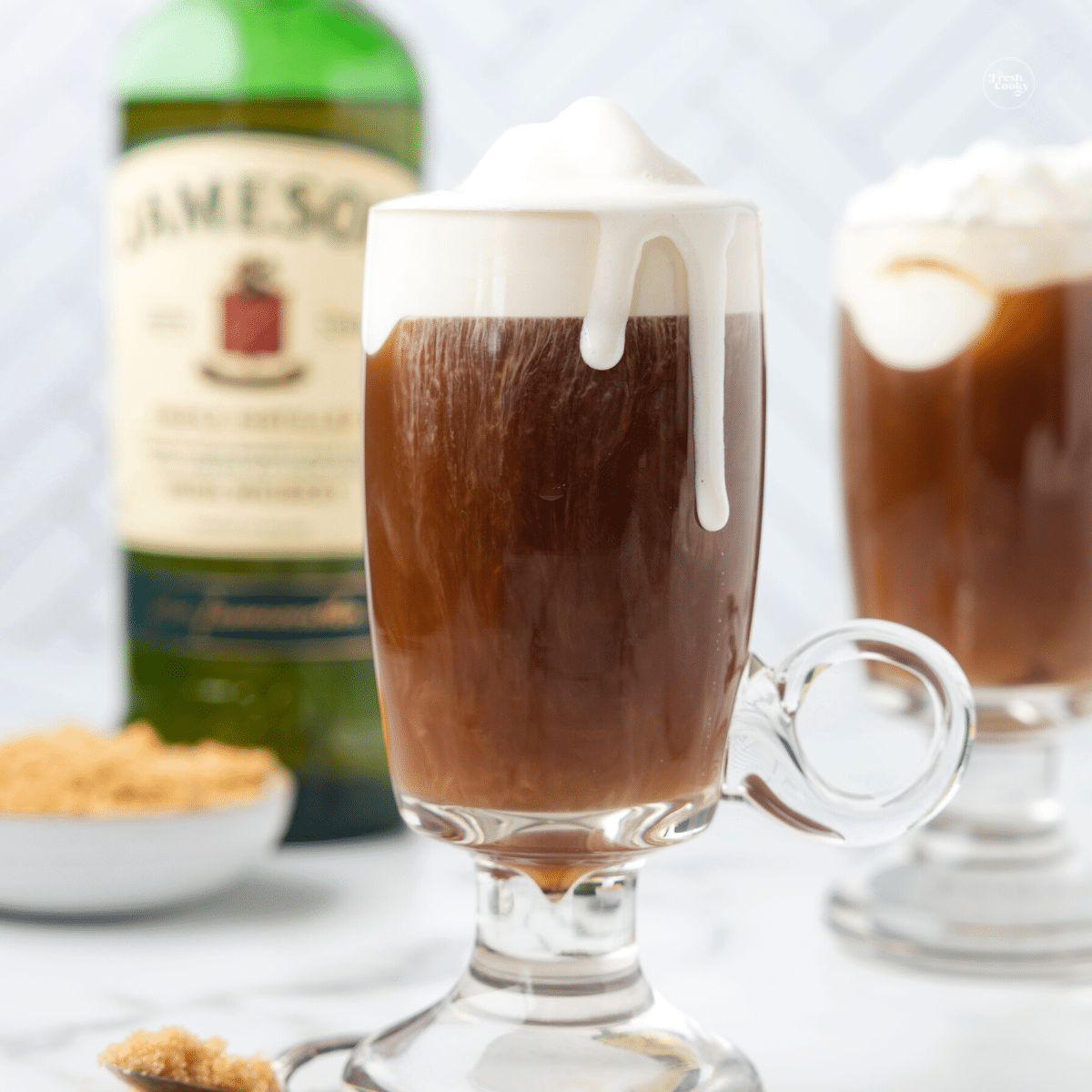Easy Irish Coffee Cocktail in glass mugs with bottle of Jameson whiskey behind. 