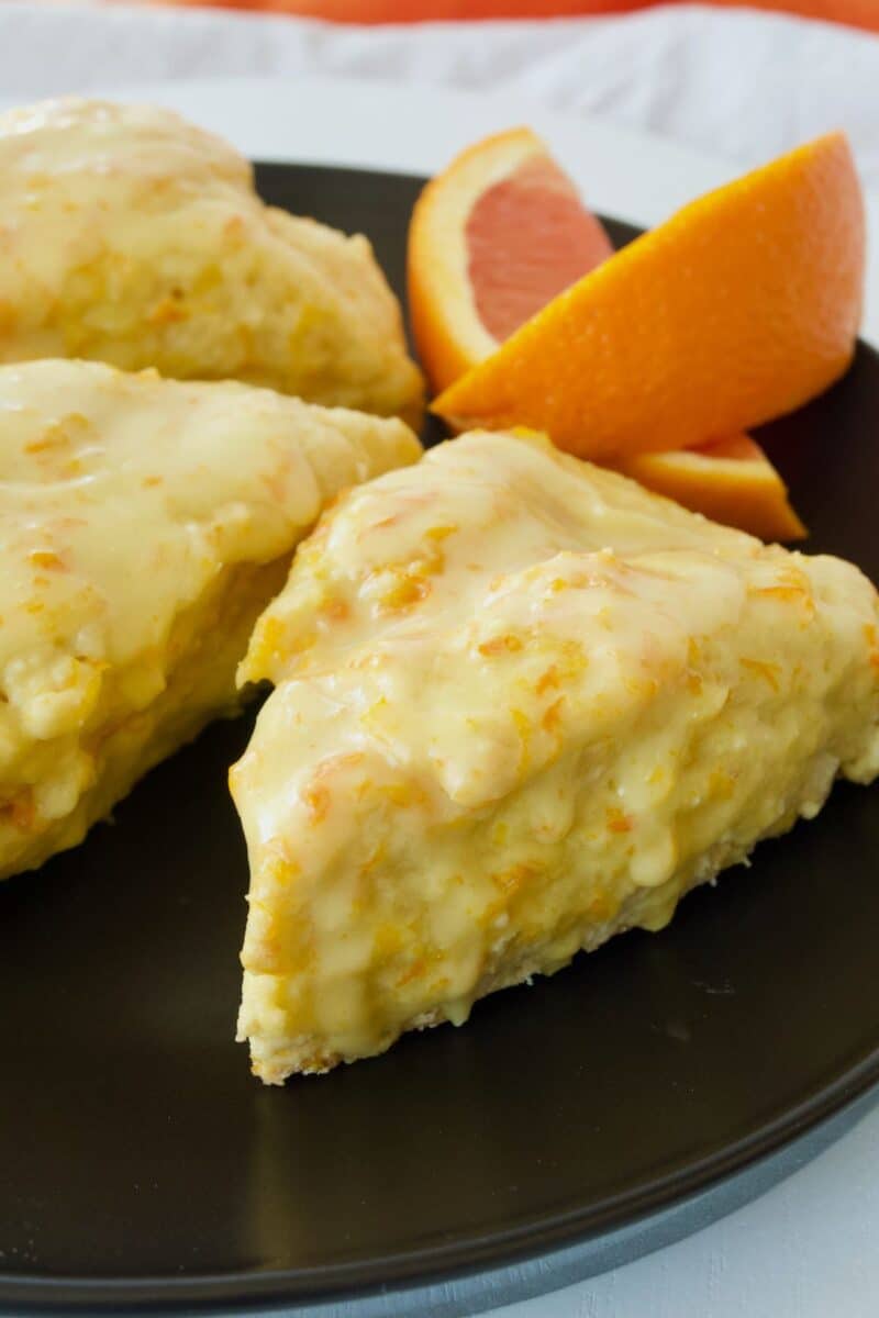 Orange scones on black plate with slices of orange.