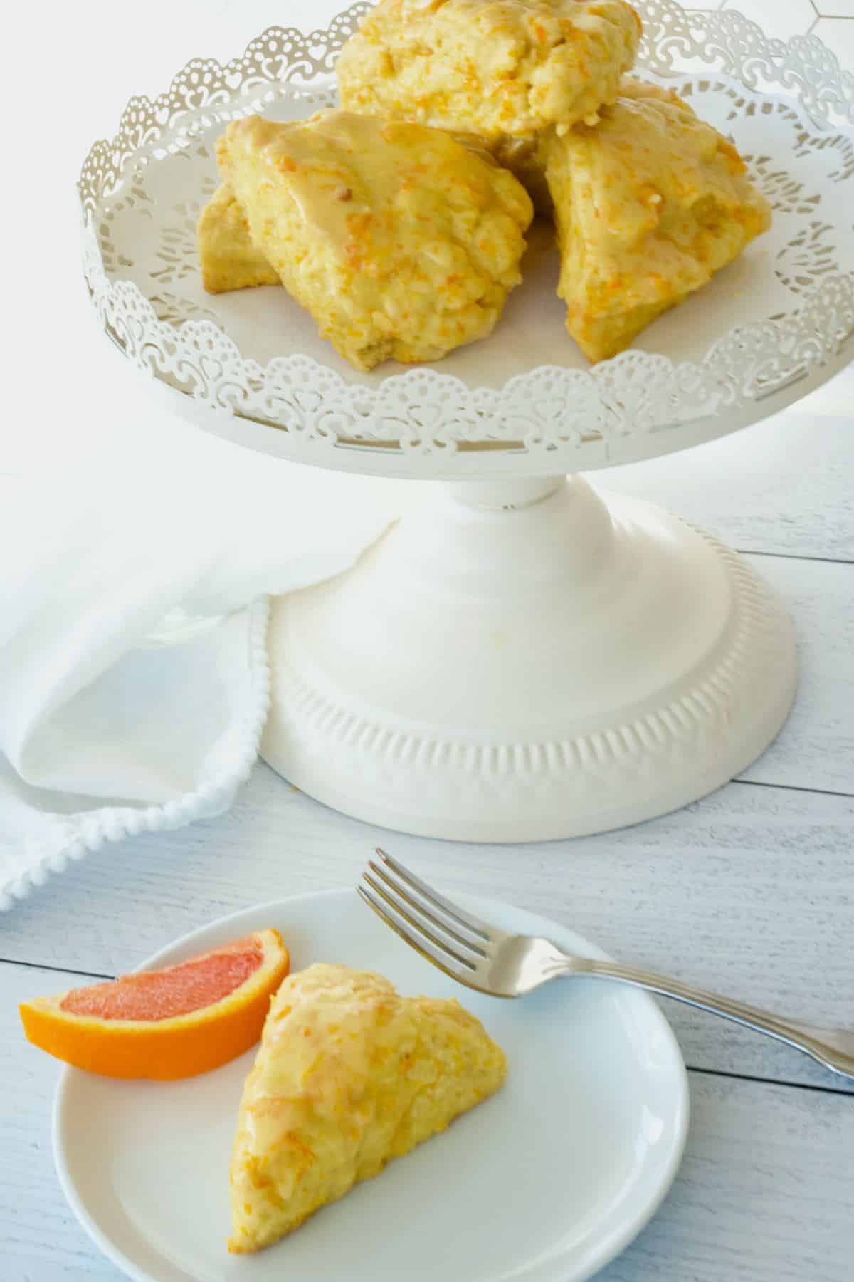 Orange scones on pedestal and one on a plate with a fork.