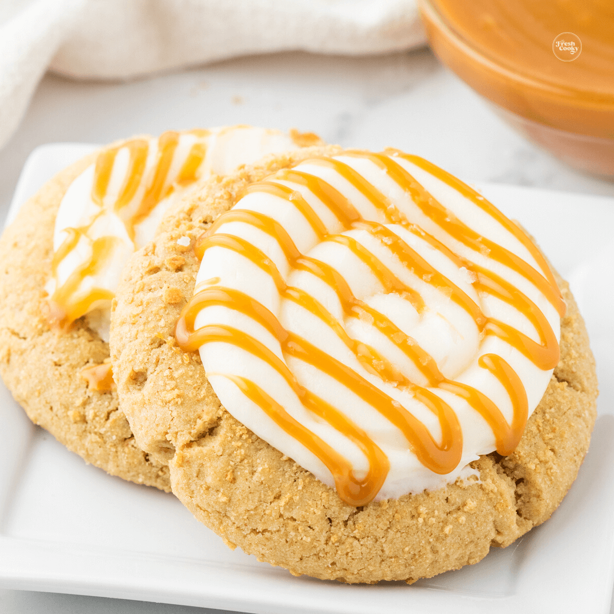 Two frosted, graham cracker cookies, topped with cream cheese frosting caramel sauce and sea salt. Salted Caramel Cheesecake cookies, crumbl copycat cookie.