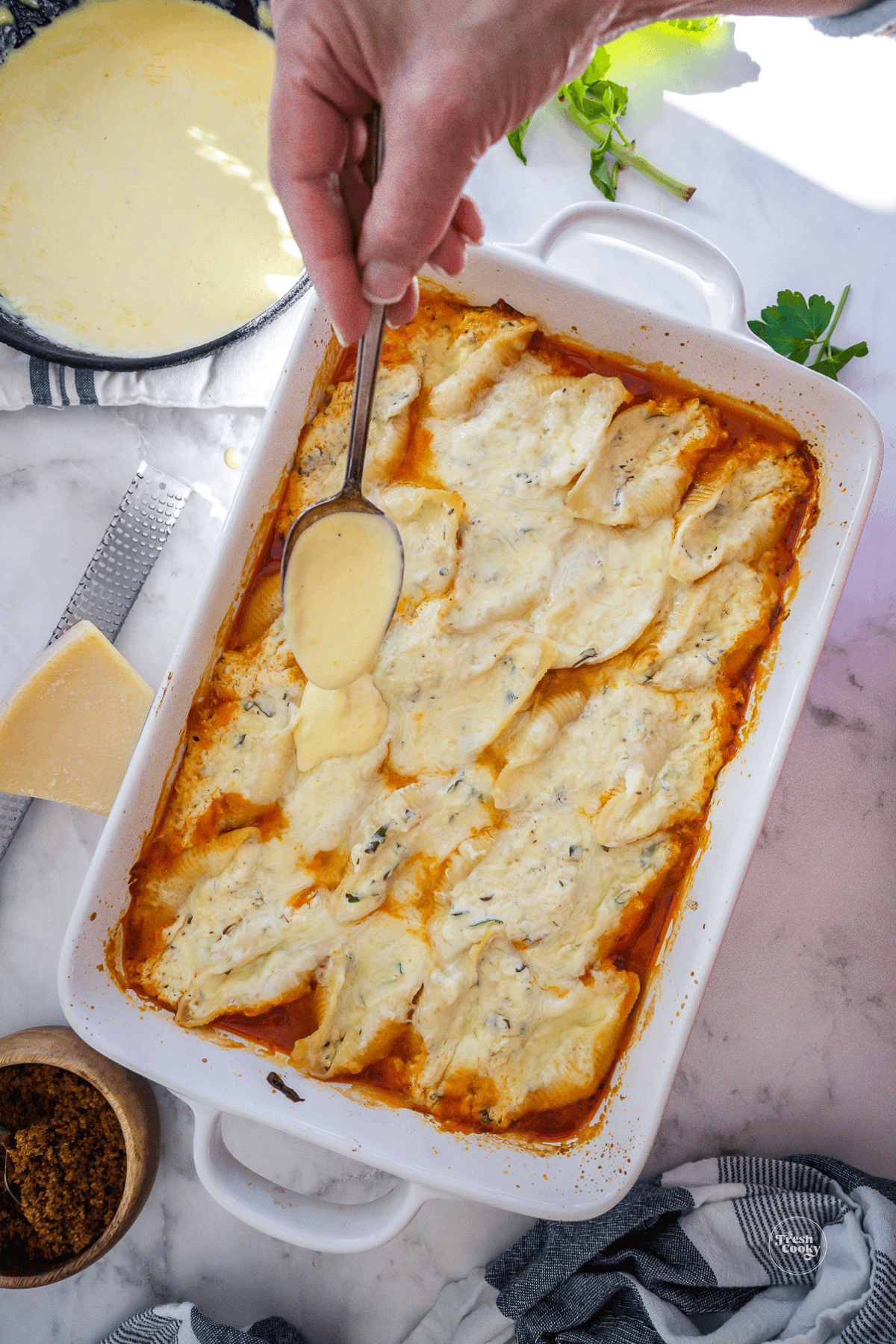 Drizzling Alfredo sauce over the top of jumbo cheese stuffed shells.