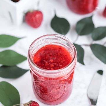 Strawberry Freezer jam in jelly jar with leaves and fresh strawberries.
