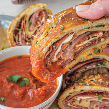 Hand dipping slice of stromboli into marinara dipping sauce.