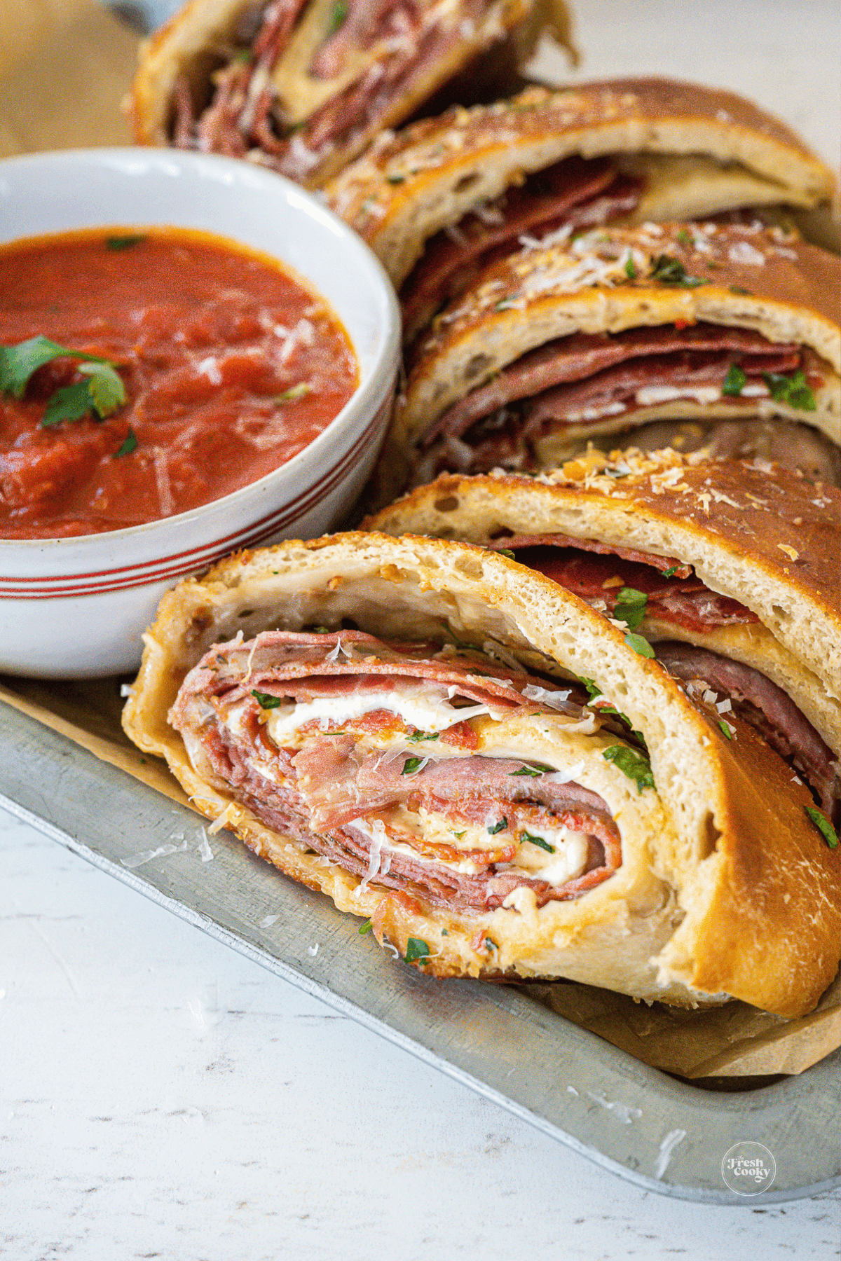 Sliced stromboli in tray with marinara dipping sauce.