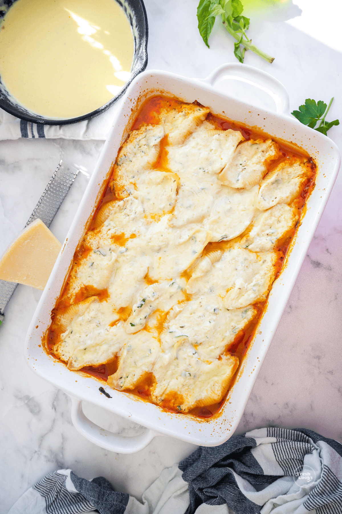 Stuffed shells baked in casserole with Alfredo sauce nearby.