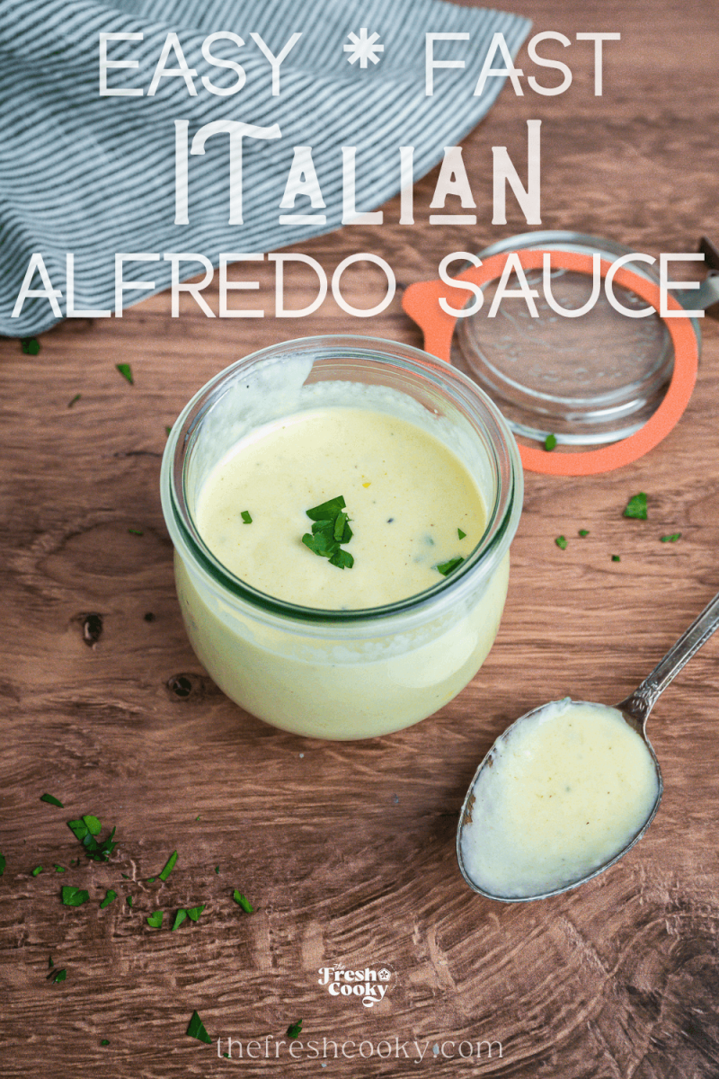 Jar on wooden table, filled with creamy, gluten-free Alfredo sauce with spoon, for pinning.