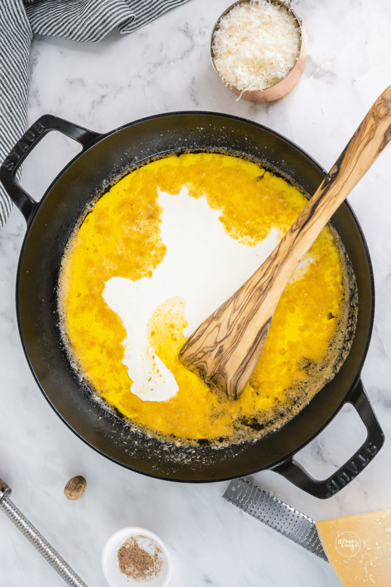 Pouring heavy cream into garlic infused melted butter. 