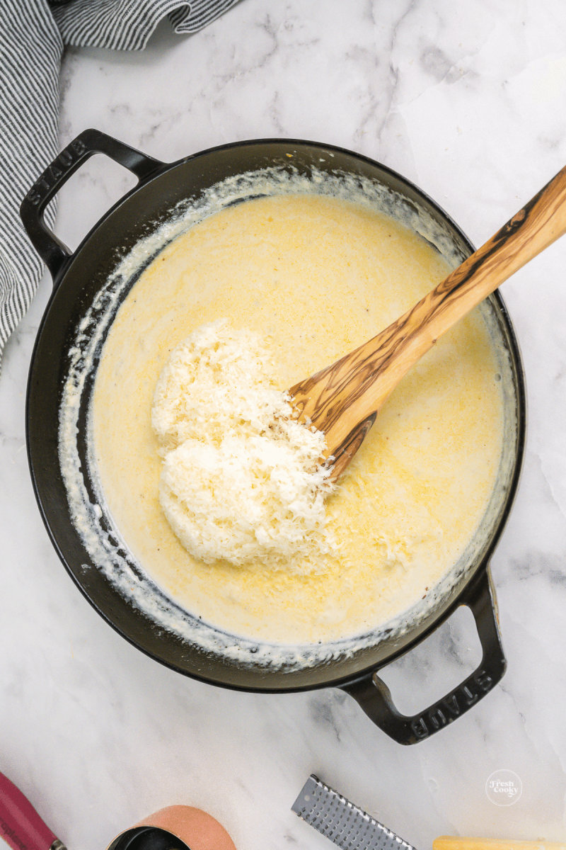 Adding fresh grated parmesan cheese to sauce, stirring in.