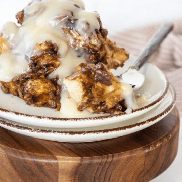 A serving of crock pot cinnamon rolls sitting on a stack of plates on a wooden trivet.