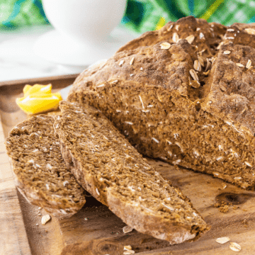 Irish brown soda bread recipe on cutting board with a few pieces sliced, butter in background.