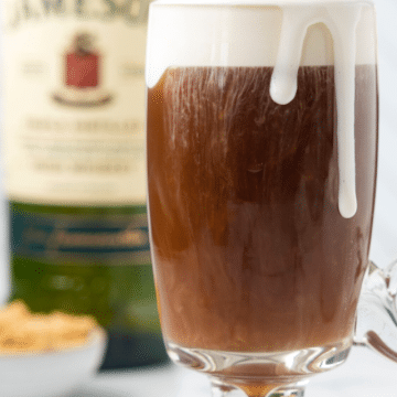 Classic Irish coffee cocktails in glass mugs topped with creamy whipped cream, Jameson whiskey bottle in background, for Facebook.