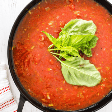Italian Marinara Sauce in a black pot with basil leaves floating on the sauce.