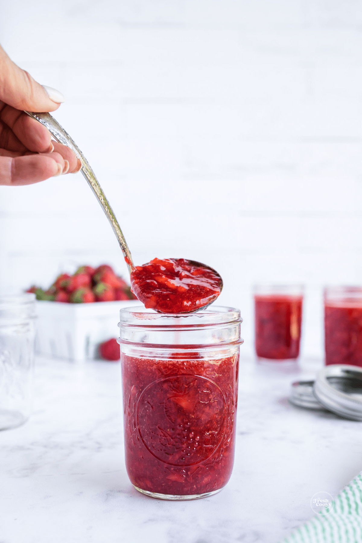 Ladling strawberry freezer jam into mason jar.