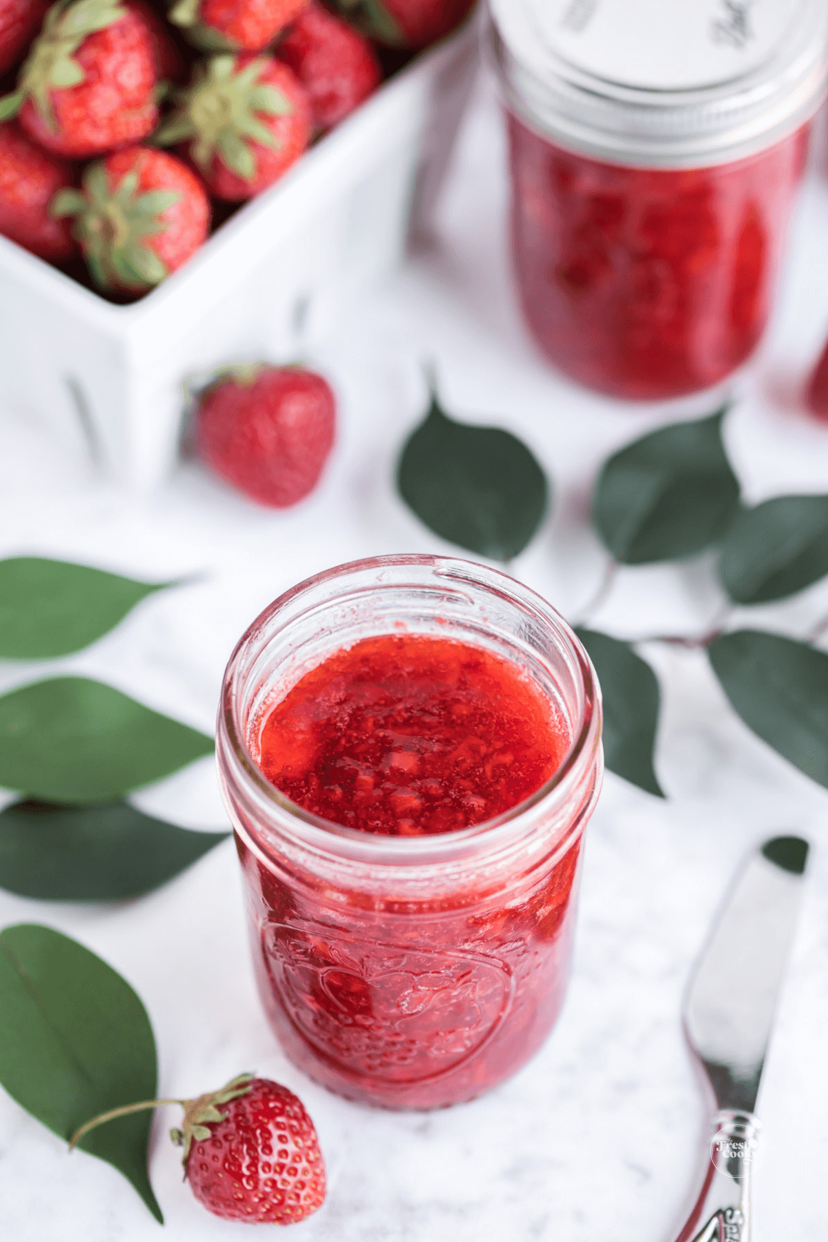 Low sugar strawberry freezer jam in a jelly jar with fresh strawberries nearby.