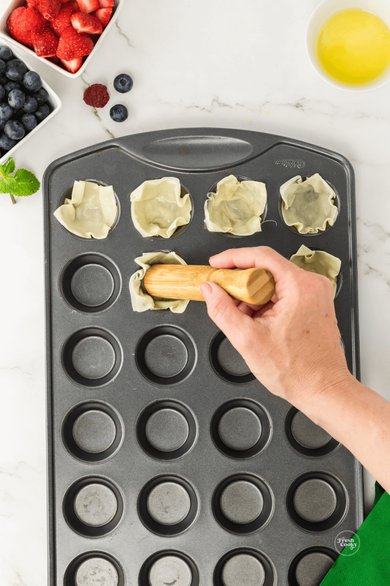 Using tamper to press phyllo pastry into mini muffin tin.