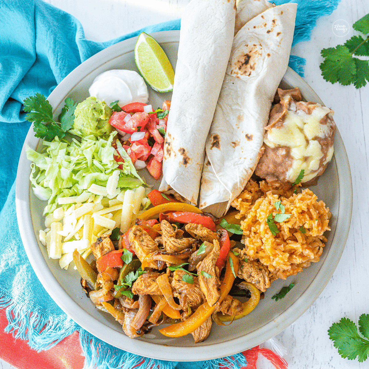 Authentic Mexican chicken fajitas on plate with tortillas, Spanish rice, beans and condiments.