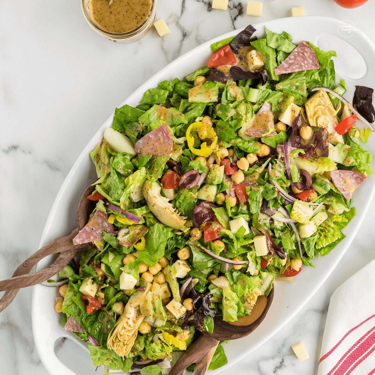 Italian chopped salad recipe in large bowl with serving utensils.