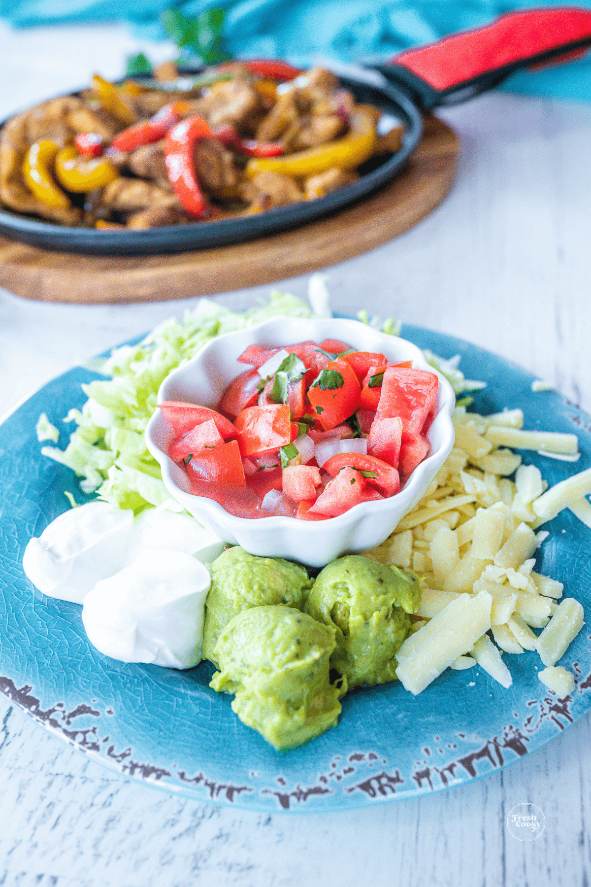 Condiments plate for chicken fajitas filled with Mexican crema, guacamole, pico de gallo, shredded lettuce and shredded cheese.