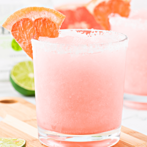 Frozen paloma cocktail in glass, with another glass behind, topped with a wedge of grapefruit.
