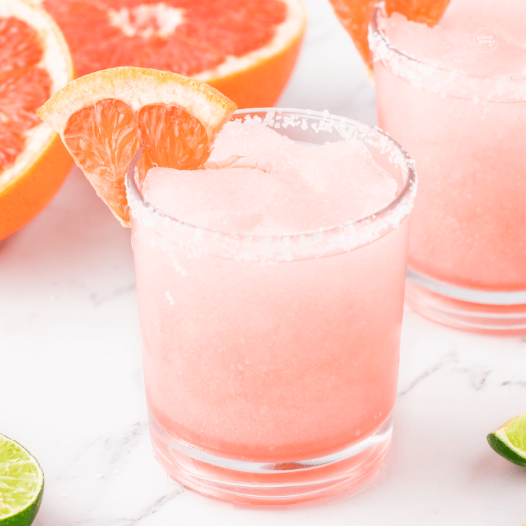 Frozen paloma cocktail in frosted, salt rimmed glass with limes and a grapefruit wedge.