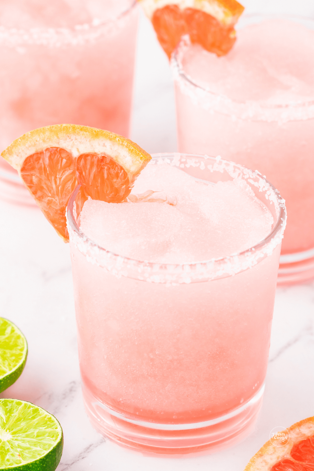 Frozen paloma cocktail in three glasses garnished with a wedge of grapefruit.