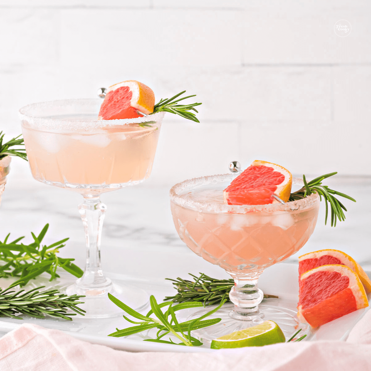 Two grapefruit mocktails, paloma spritzer in pretty coupe glasses, garnished with rosemary and grapefruit.