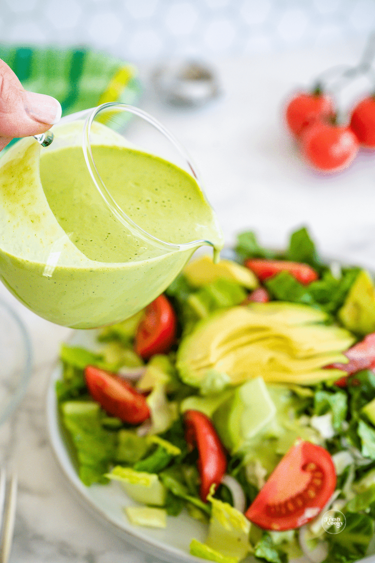 Pouring green goddess salad dressing onto a fresh green salad.