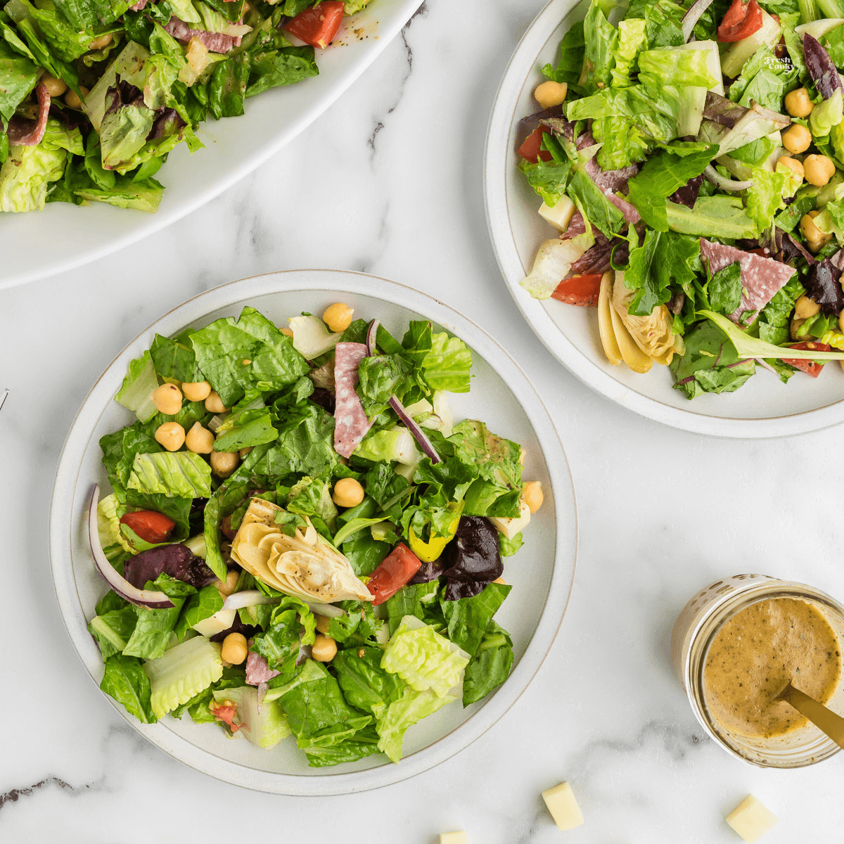 Plates of Italian Chopped Salad with zest Italian dressing on the side.