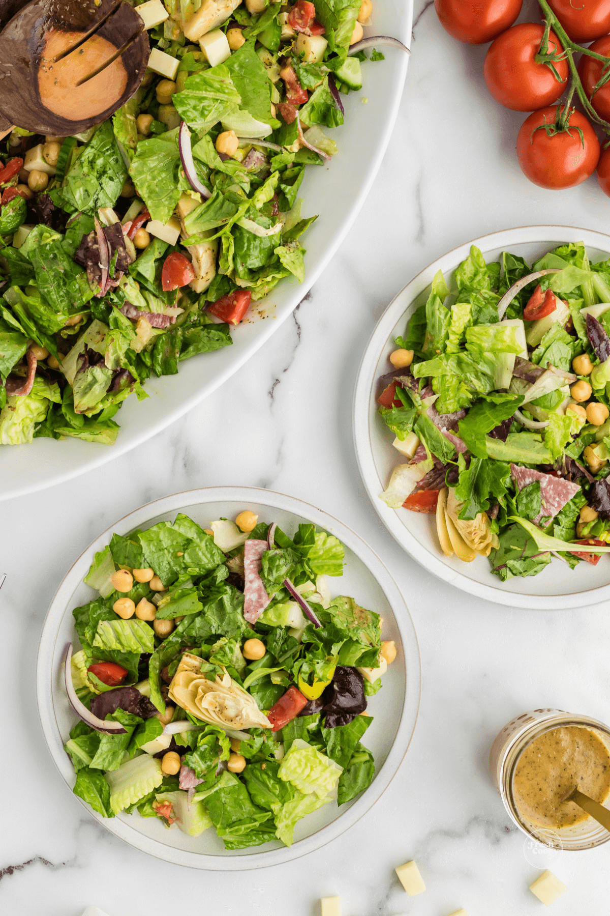 Italian Chopped salads in large bowl and two served in plates with zesty italian dressing on the side.