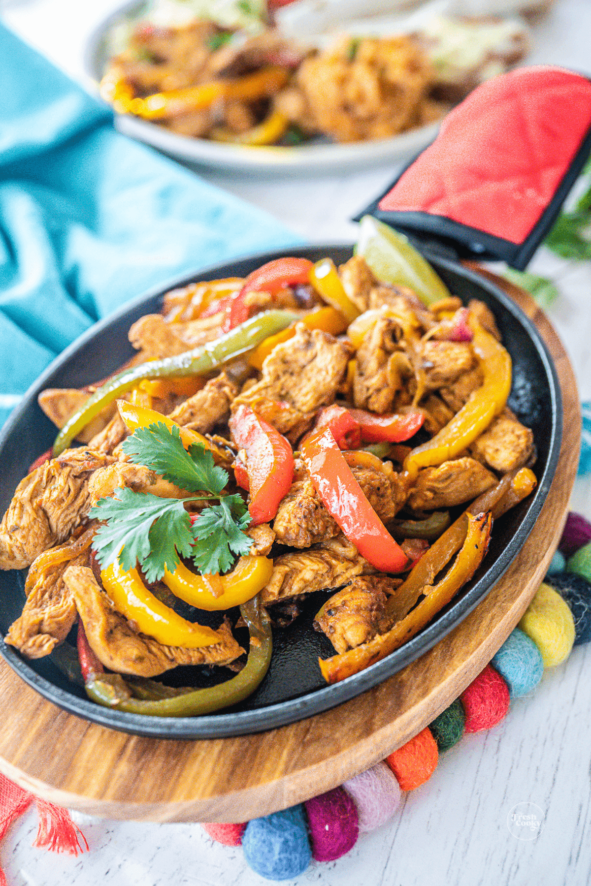 Sizzling skillet filled with Mexican chicken fajitas with sides in background.