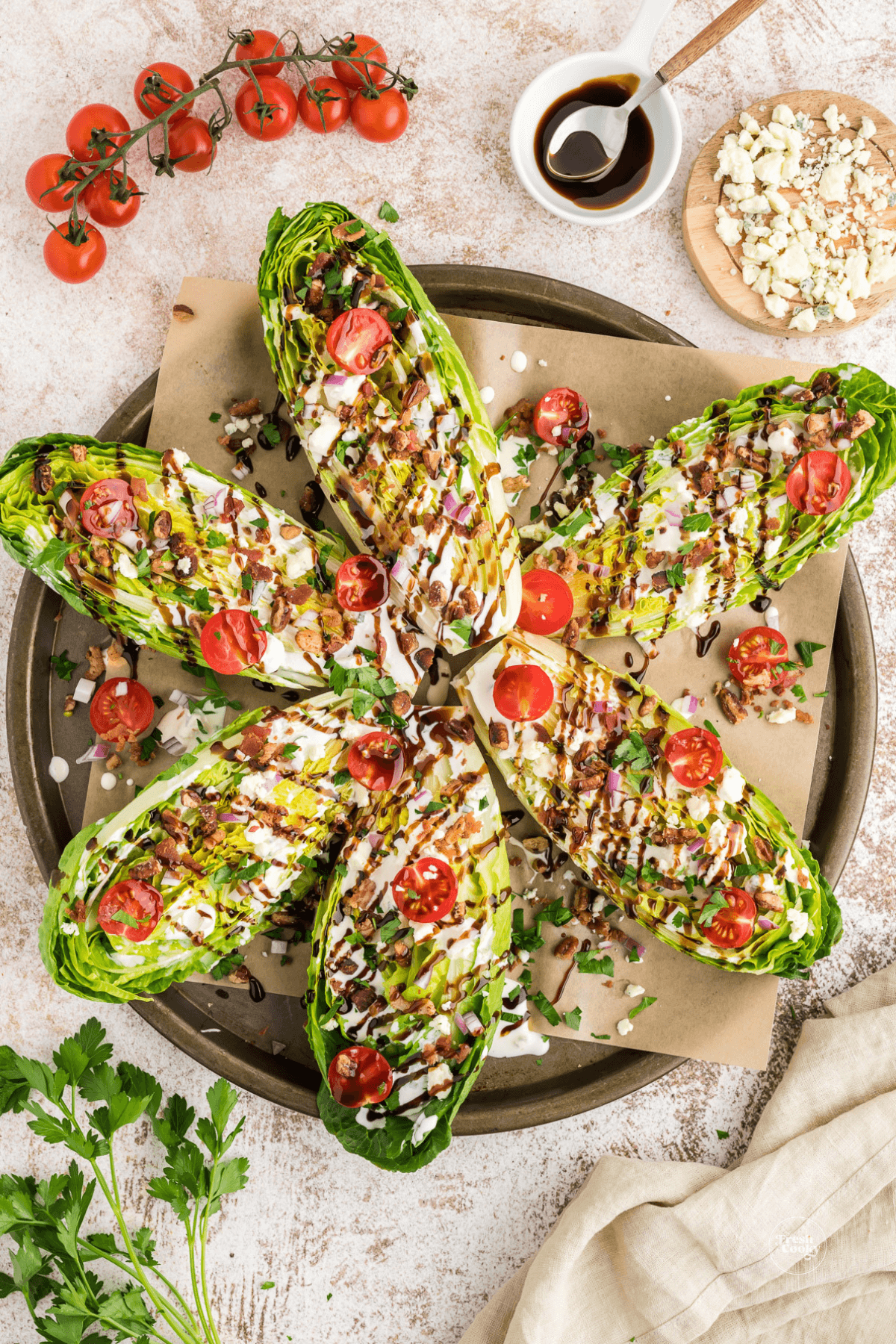 Romaine wedges all dressed with blue cheese dressing, toppings and blue cheese crumbles on a round platter, perfect for serving at a party.