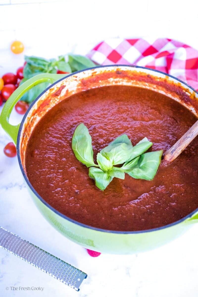 A large pot of homemade spaghetti sauce with wooden spoon and fresh basil.