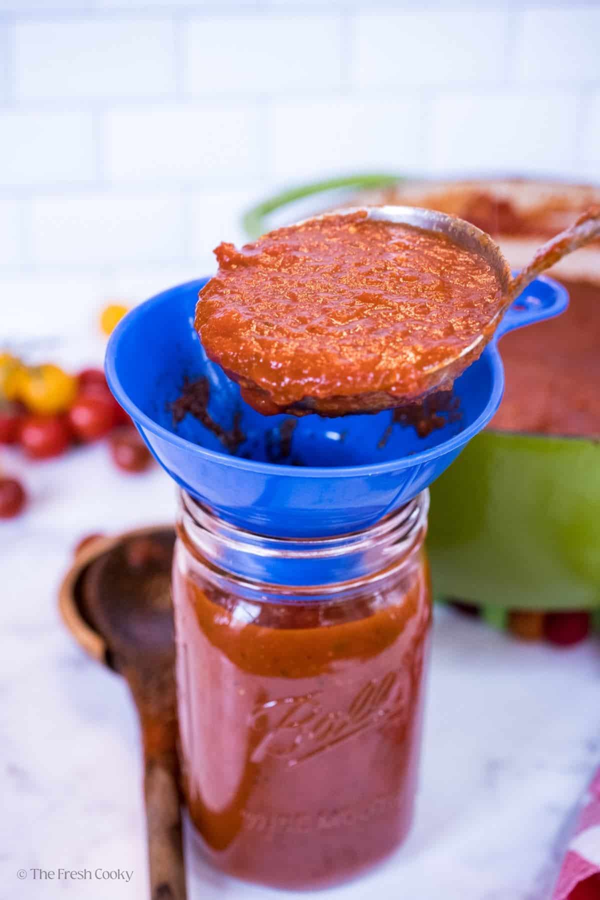Spooning spaghetti sauce into a glass jar. 