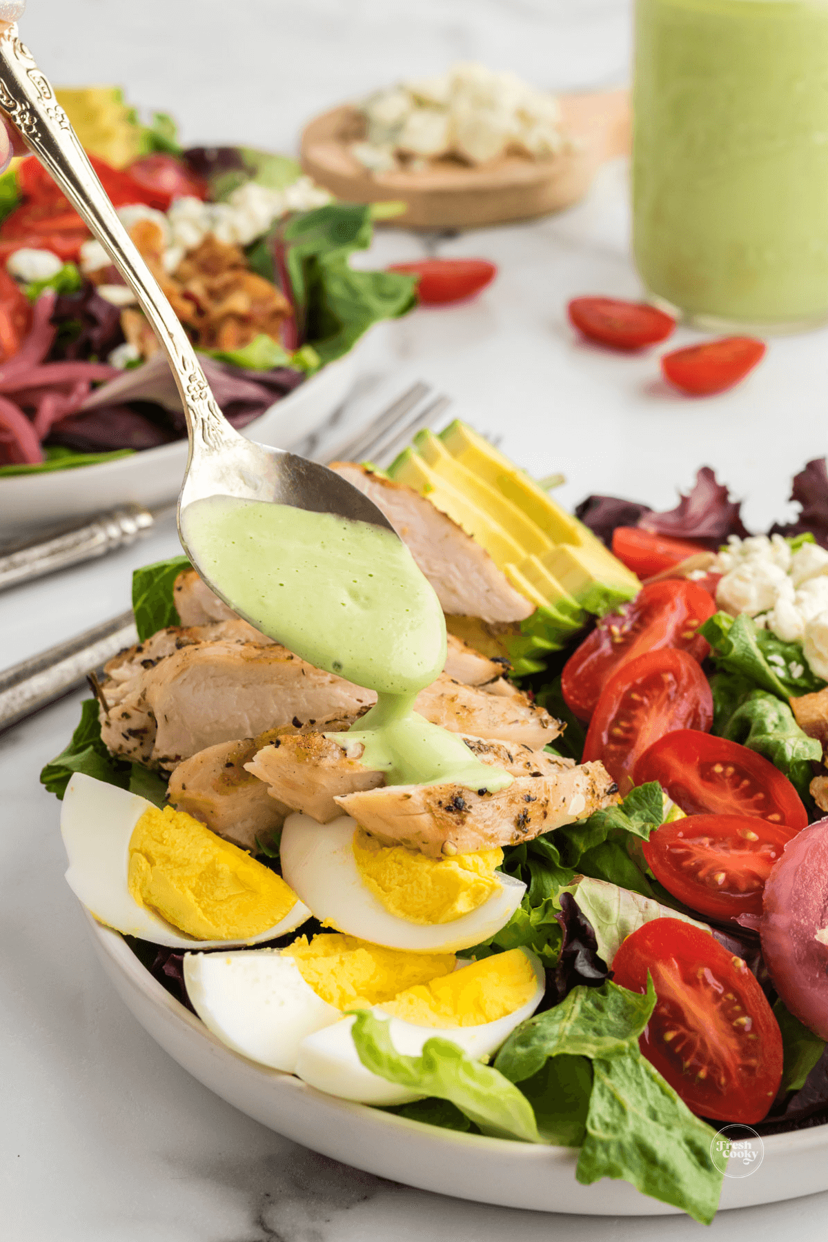 Drizzling green goddess dressing onto fresh made chicken cobb salad.