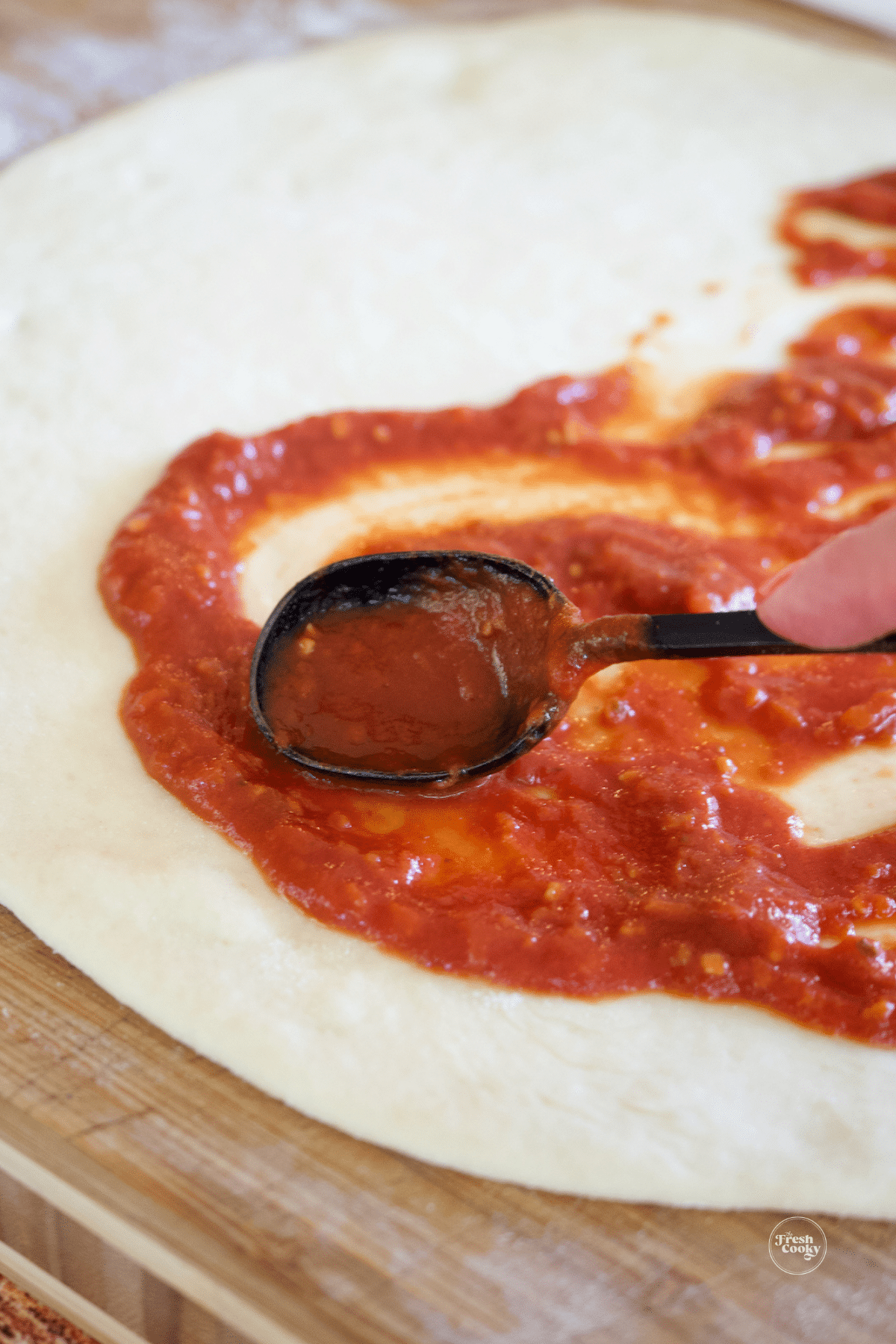 Spreading pizza sauce onto pizza dough.