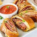 Slices of stromboli on a square white plate with a ramekin of marinara sauce.