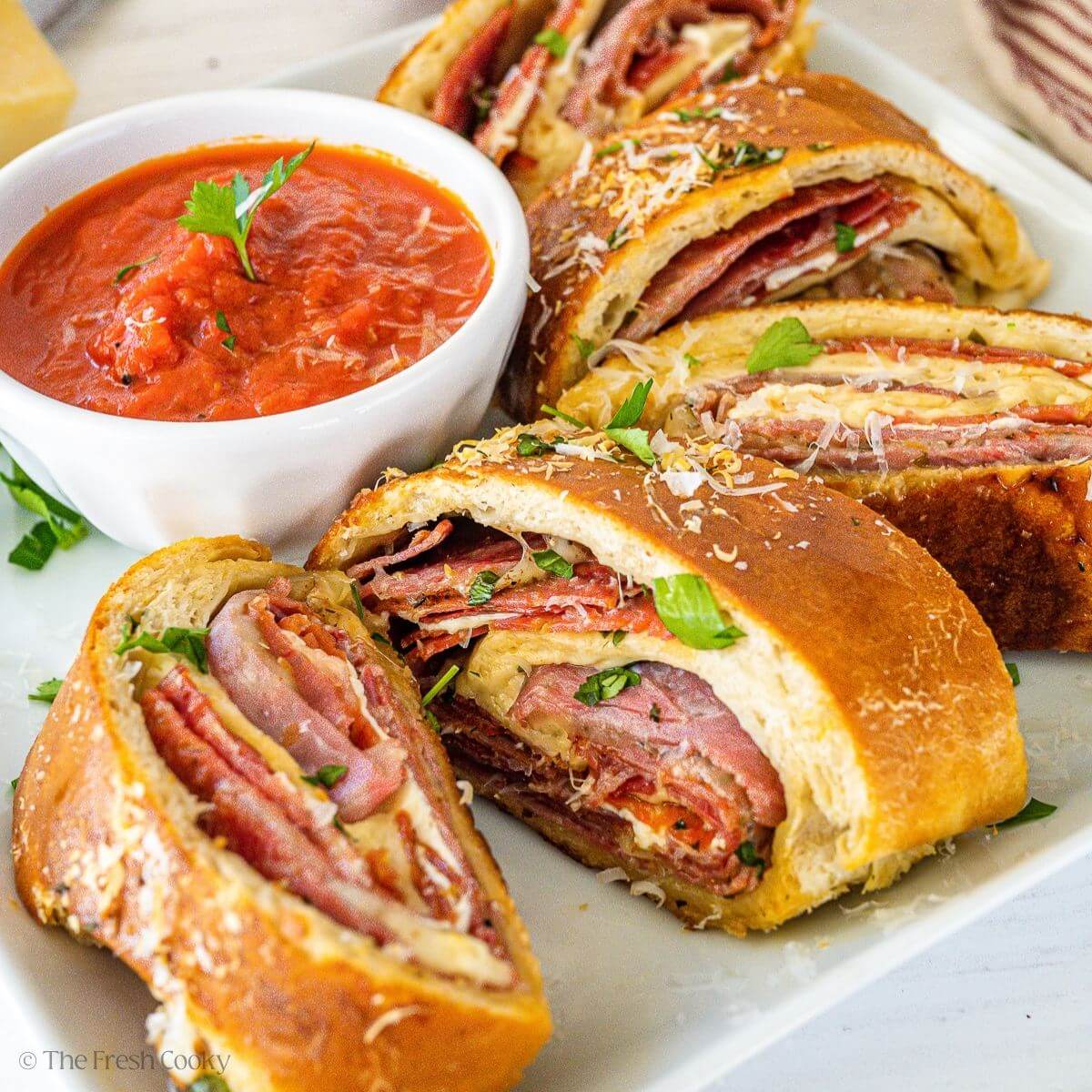 Slices of stromboli on a square white plate with a ramekin of marinara sauce.