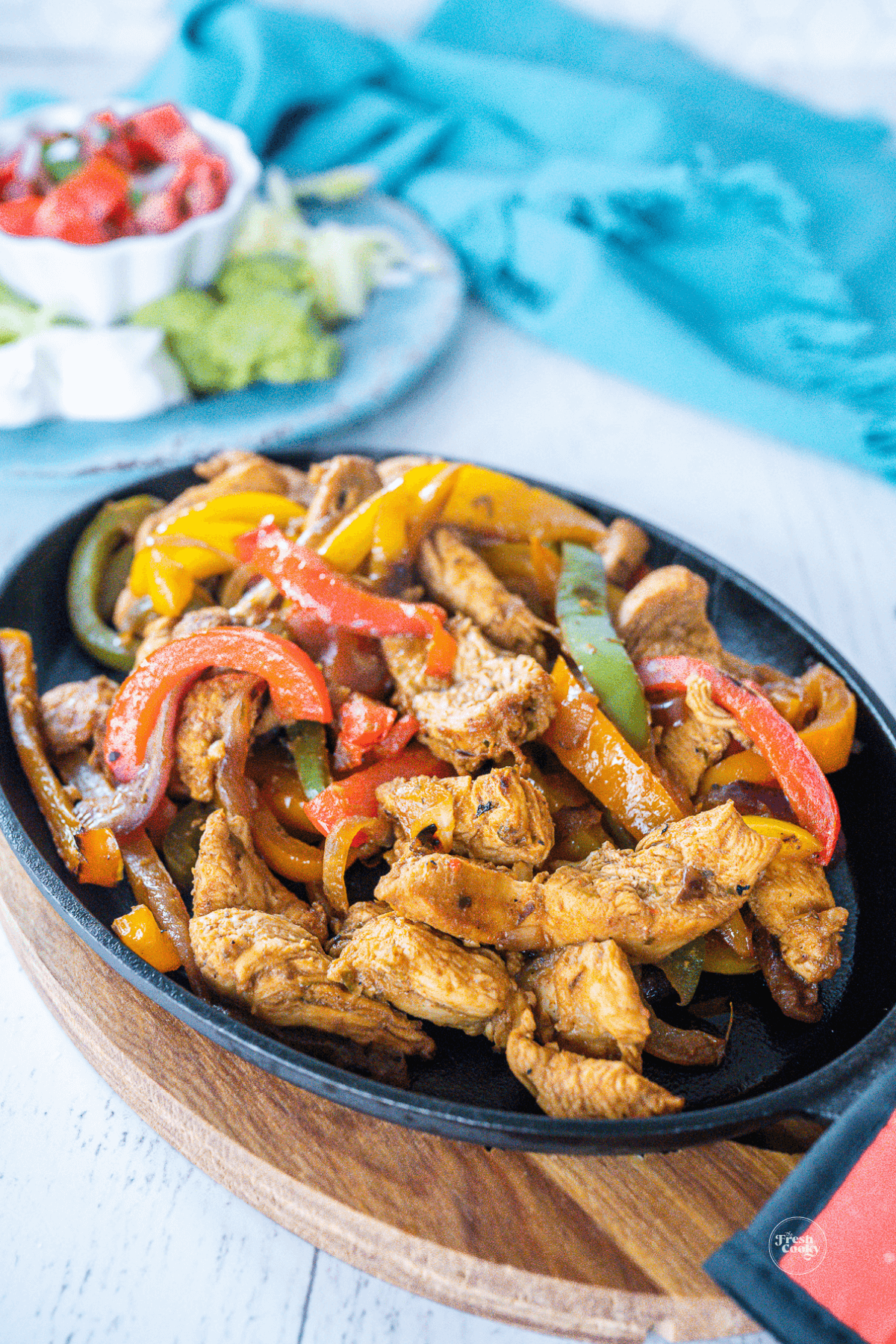 Authentic Mexican chicken fajita recipe in cast iron skillet with toppings in the background. 