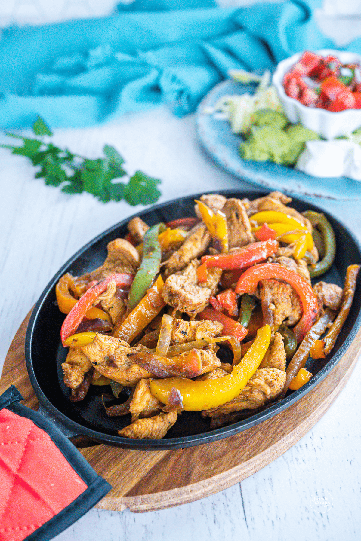 Authentic Mexican chicken fajita recipe in a skillet with onions and peppers and condiments behind.