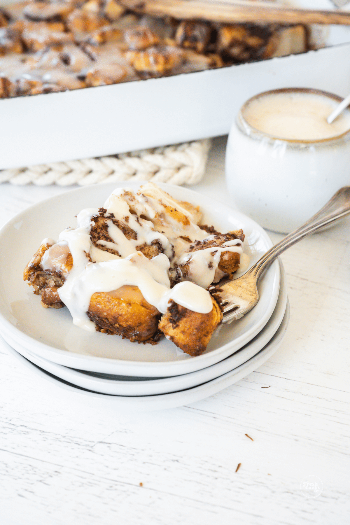 Slice of cinnamon roll casserole on plate with a fork-filled bite.